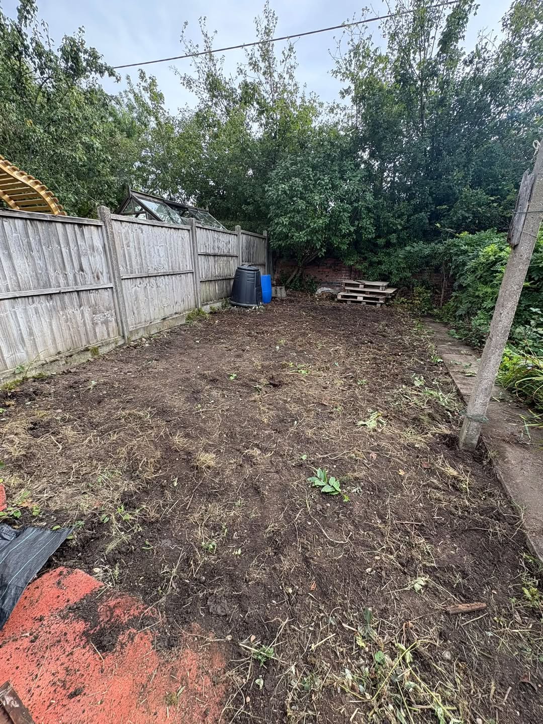 The image shows a back garden with a clear soil finish, replacing what used to be covered in weeds amd bramble.