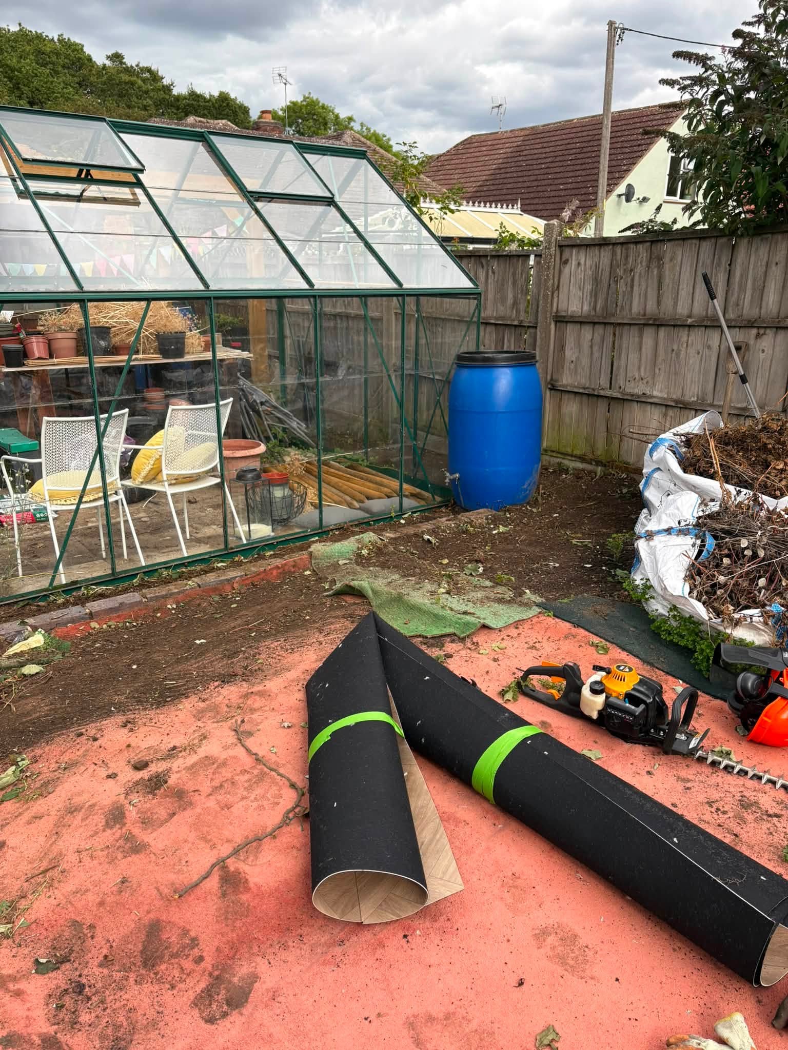 The area around a garden greenhouse was overcome with weeds, which have all been stripped back to make the soil bed usable again.